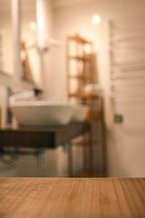 Wooden countertop in the foreground with a blurred view of a modern bathroom featuring two white...
