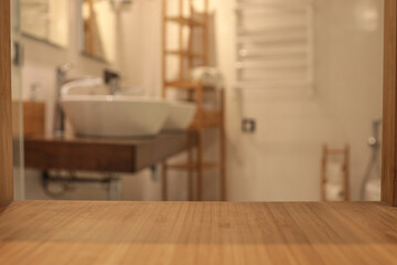 Wooden countertop in the foreground with a blurred view of a modern bathroom featuring two white...