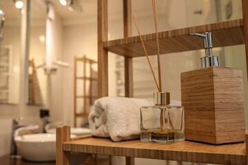 Bright modern bathroom interior with wooden shelving, rolled towel, fragrance diffuser, and soap...