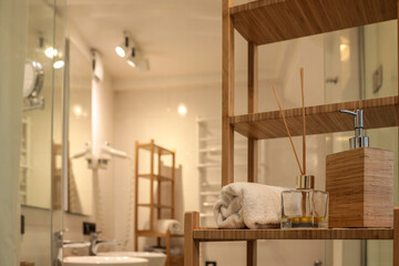 Bright modern bathroom interior with wooden shelving, rolled towel, fragrance diffuser, and soap...