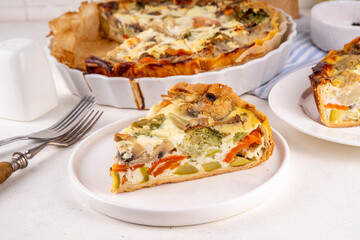 Slice of freshly baked homemade pie quiche lorraine on white table, top view, copy space. Vegan quich tart pie with mushrooms, tomatoes, zucchini, spinach and cheese