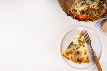 Slice of freshly baked homemade pie quiche lorraine on white table, top view, copy space. Vegan quich tart pie with mushrooms, tomatoes, zucchini, spinach and cheese