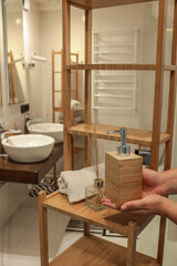 Woman's hands placing a wooden soap dispenser on a bamboo bathroom shelf. Minimalist spa decor with...
