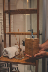 Woman's hands placing a wooden soap dispenser on a bamboo bathroom shelf. Minimalist spa decor with...