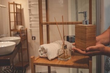 Woman's hands placing a wooden soap dispenser on a bamboo bathroom shelf. Minimalist spa decor with...