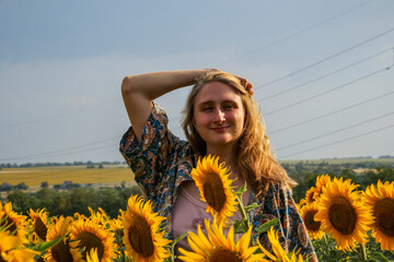 young blond woman among sunflowers in the field, doing her hair, straightening her hair with her hands, waist-length portrait, large yellow flowers