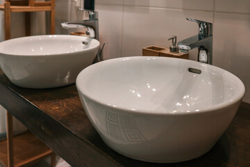 Modern white ceramic washbasins with chrome faucets on wooden countertop in a stylish bathroom interior