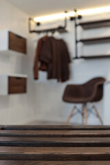 Close-up of dark wooden slats with a blurred background showing a modern interior featuring floating drawers, a brown chair, and hanging clothes in a cozy, industrial-style room