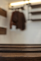Close-up of dark wooden slats with a blurred background showing a modern interior featuring floating drawers, a brown chair, and hanging clothes in a cozy, industrial-style room