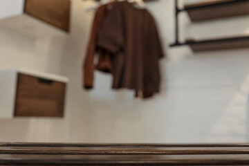 Close-up of dark wooden slats with a blurred background showing a modern interior featuring floating drawers, a brown chair, and hanging clothes in a cozy, industrial-style room