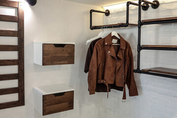 Stylish brown suede jacket and t-shirt hanging on minimalist black metal pipe rack in a cozy modern...