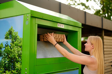 woman recycling cardboard using green disposal unit emphasizes eco-friendly practices. highlights...