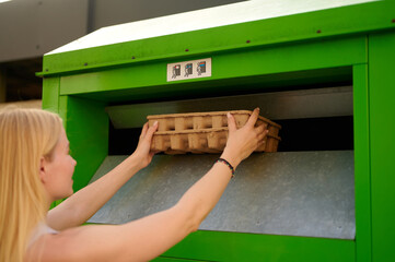 woman recycling cardboard in green bin promotes eco-friendly waste management. environmental...