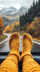 Legs in yellow socks rest on a car dashboard overlooking rainy mountain road