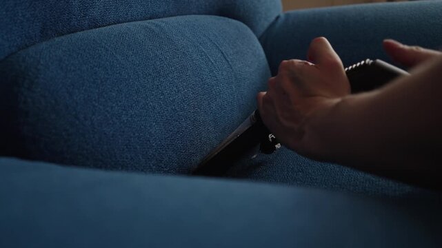 Close-up unrecognizable man using washing vacuum cleaner with upholstery nozzle to remove dust and dirt from blue sofa, ensuring thorough and effective cleaning of furniture, close-up, slow motion.