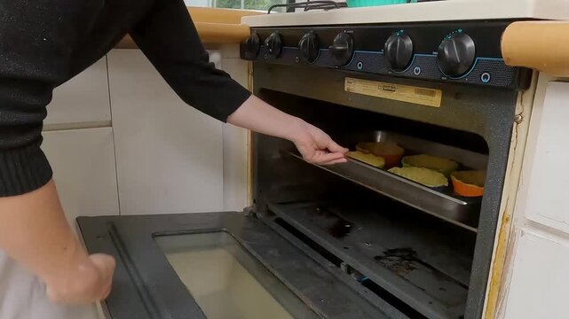 Professional female chef positioning mini quiches on metal tray, baking home-style lunch with culinary skill in modern kitchen environment