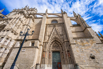 Sevilla Cathedral in Spain features a grand Gothic entrance with intricate details under a blue...