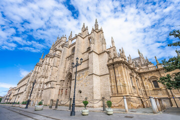 Fototapeta premium A wide-angle perspective captures the majestic and intricate exterior of Seville Cathedral, a UNESCO World Heritage site, under a dramatic blue sky with white clouds in Spain.
