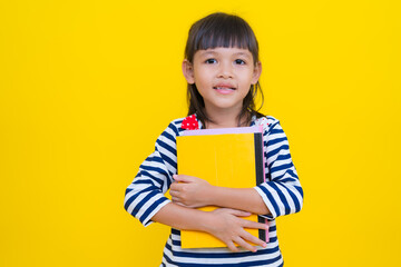 Cute asian girl holding books on yellow background: education and childhood concept