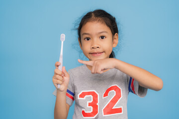 Happy little girl holding toothbrush promoting oral hygiene on blue background
