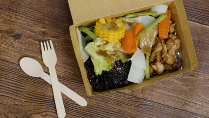 Disposable wooden cutlery is placed near a cardboard takeaway box containing black rice, teriyaki...