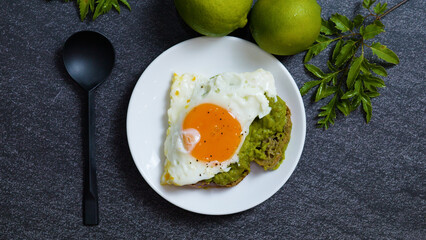 Healthy wholemeal bread toast topped with creamy mashed avocado and a perfectly fried egg, garnished with lime, all presented on a dark slate background from a top view angle