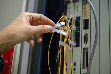 Network technician performing inspection on fiber optic cables in server room with hand holding...