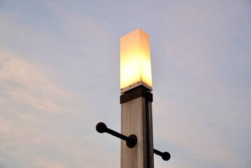 A glowing wooden lamp post captured at dusk with a soft, pastel sky in the background. The warm...