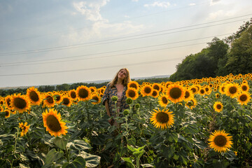 young blonde woman standing in sunflower field, full face, distant view, waist-length portrait, large yellow flowers, posing, smiling, summer, model, 
