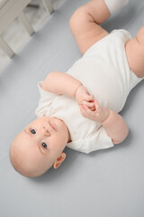 Cute newborn baby in bodysuit lying on back in crib, playing, smiling, looking at mom close-up....