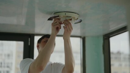 Portrait of electrician young man replacing light bulb in ceiling light fixture, close-up, slow motion. Concept of optimal illumination for indoor space performing essential maintenance, repair work. - Powered by Adobe