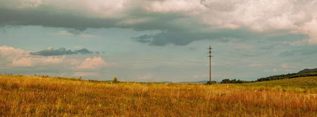 Electrical power line pole in a field in Europe. Partially cloudy summer day, no people