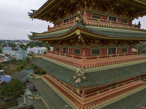 Aerial view of the intricate, multi-tiered pagoda with its vibrant red and gold trim contrasting against the muted green roof tiles, Pleiku, Gia Lai, Vietnam.