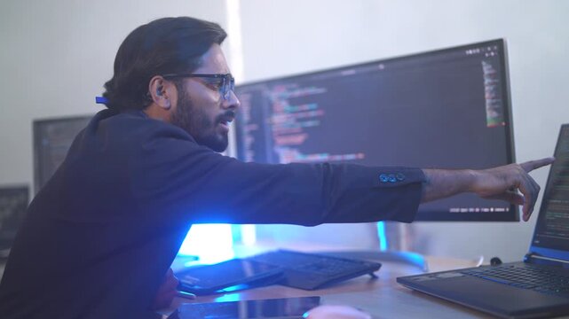 Indian male software architect developing a neural network framework. Focused programmer writing optimized code for a deep learning algorithm at a multi-display workstation.