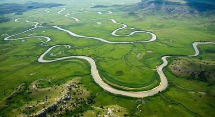 Aerial view showcases a winding river flowing through vibrant green grasslands under a clear sky.