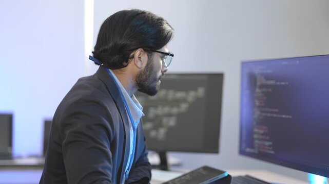 Indian male software architect developing a neural network framework. Focused programmer writing optimized code for a deep learning algorithm at a multi-display workstation.