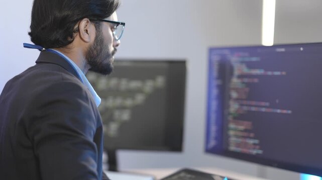 Focused Indian male AI developer coding a complex machine learning algorithm late at night. A dedicated data scientist working on a neural network at a multi-moni