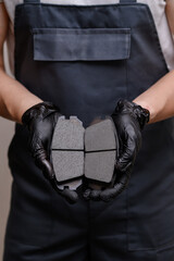 Auto mechanic in black gloves holding two brake pads in hands demonstrating them, close-up. Concept...