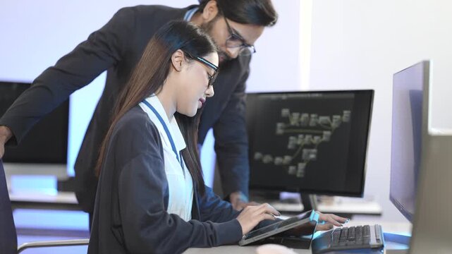 Diverse IT professionals collaborating in a command center. A male programmer explains data on a tablet to a female developer working on code at her computer.