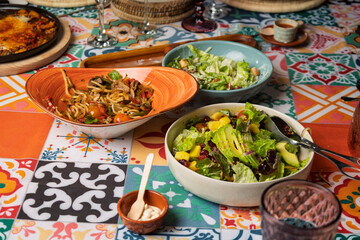 Colorful table setting featuring noodles, caesar salad, and mango avocado salad