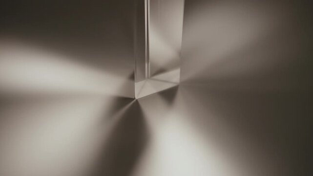 Close-up of light refracting through triangular glass prism, creating spectrum of colors and casting shadow on table in dark room. Concept principles of optics and light dispersion, slow motion.