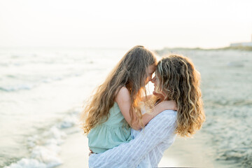 Young mother with little daughter near the sea. Beach with sand. Blue water.