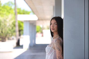A young, attractive Latin woman with tattoos on her arms and dressed in casual clothes leans her...