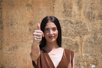 Young and beautiful woman in a successful pose with her thumb up and smiling on a brown background.