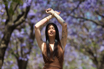 A young, attractive Spanish woman with dark hair, tattoos, long hair, a brown dress, and black...