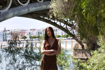 A young, attractive Spanish woman with long brown hair, wearing a brown dress and black boots,...