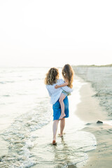 Young mother with little daughter near the sea. Beach with sand. Blue water.
