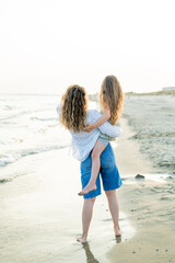 Young mother with little daughter near the sea. Beach with sand. Blue water.