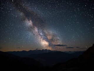 Dramatic milky way sparkles above dark mountain silhouettes at night