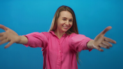 Young caucasian woman in pink shirt extending arms for hug against isolated blue background wall...